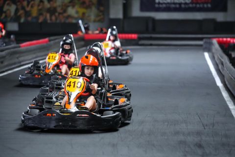 Copii cu căști colorate în karturi, unul după altul pe circuitul indoor Red Motor