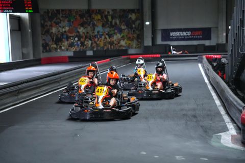 Pluton de karturi în cursă pe circuitul indoor Red Motor, cu panoul de cronometraj în fundal